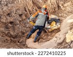 Small photo of A worker compacts soil or sand with a vibrating plate in a trench at a construction site close-up. Vibratory soil compaction for laying underground utilities