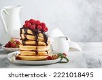 Small photo of American pancakes. Stack pancakes with fresh raspberry with chocolate glaze or toppings in white bowl on light gray table background. Homemade classic american pancakes. Magazine concept. Top view.