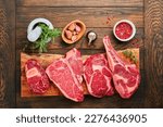 Small photo of Raw prime steaks. Variety of fresh black angus prime meat steaks T-bone, New York, Ribeye, Striploin, Tomahawk cutting board on black or dark background. Set of various classic steaks. Top view.
