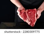 Chef cutting steak beef. Mans hands hold raw steak T-Bone on rustic wooden cutting board on black background. Cooking, recipes and eating concept. Selective focus.