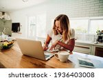 Caucasian female student working from home writing in note pad with laptop sitting next to hot coffee