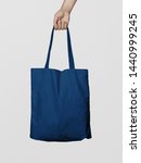 Small photo of Hand Holding Fabric Canvas Tote Bag or Goodie Bag Isolated on Blue Navy Colour Background