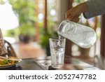Waiter hand pouring water with ice into glasses on table