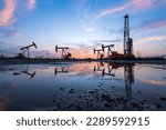 Small photo of Oil field site, in the evening, oil pumps are running, The oil pump and the beautiful sunset reflected in the water, the silhouette of the beam pumping unit in the evening.