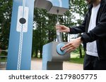 Small photo of Man refilling his water bottle at the city. Free public water bottle refill station. Sustainable and green city. Male in black coat. Tap water to reduce plastic bottle usage. Drinking water dispenser