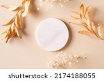 Dry natural grass, leaves and flowers frame with white marble podium, beauty and fashion concept mock up on beige background flat lay, top view, copy space