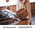 Man pouring water onto hot stone in sauna room. Steam on the stones, spa and wellness concept, relax in hot finnish sauna.