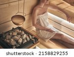 Woman relaxing in wellness spa, sweating in Finnish sauna, focus on sauna stove.