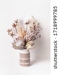 Small photo of Beautiful dried flower arrangement in a stylish ceramic white vase with brown aztec pattern. Dried flowers include pink proteas, banksia, gold palm leaf, kangaroo paw, cotton and ruscus leaves.