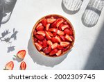 Top view of summer strawberry pie on white table with beautiful hard shadows of glass goblet