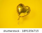 Single gold heart shaped foil balloon for birthday on yellow background. Holiday celebration. Valentine's Day party decoration. Love concept.