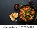 Bigos - traditional dish of polish cuisine,stewed cabbage with meat, sausage and dried mushrooms in a pan on a black slate, stone or concrete background. Top view with copy space.