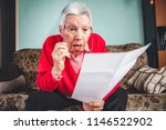 Small photo of Senior old woman shocked with the bills she receives, appalled and gasping