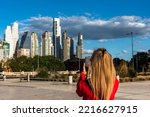 Mature blonde adult woman taking a smartphone photo of a group of buildings in the Puerto Madero area, Buenos Aires.