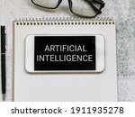 Phrase ARTIFICIAL INTELLIGENCE written on smartphone with pen,note book and eye glasses. IT concept.
