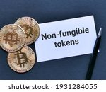 Phrase NON FUNGIBLE TOKENS written on white card with bitcoins isolated on black background. Cryptocurrency and finance concept.