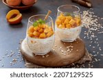 Small photo of Peach Overnight Oats. Healthy breakfast or dessert made with oat grain soaked for the night in milk or yogurt topped with cubes of fresh peaches, served in a clear glasses. Dark, selective focus