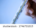 Thermometer in a woman's hand isolated on clean background. Temperature measuring. Blue toning. Close up.