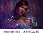 Small photo of Artistic portrait of a beautiful girl with silver make-up. On a dark background in purple tones and whitish. in a colored dress made of transparent color film