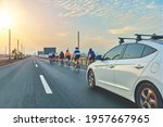 Group of professional cyclists training on highway with safety escort car. A group of cyclists followed by team cars