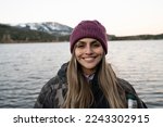 Portrait of a young woman smiling. The placid lake and mountain range in the background. Beautiful sunset colors in the environment.