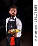 Small photo of Charismatic flunky helpfully holds cooked dish on a black background.