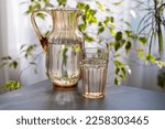 Small photo of a decanter and a glass of drinking water stand on a table by the window next to home plants