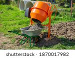 concrete is loaded into a cart from a 200 liter orange electric concrete mixer, photo taken on a sunny summer day outdoors
