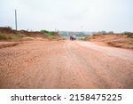 Two men walking on wet red soil path or road with cycle.