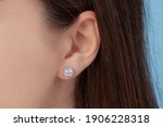 Round silver earrings on the ear of a well-groomed lady on a blue background