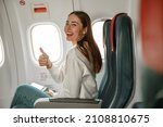 Cheerful young woman doing thumbs up gesture in plane