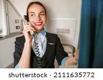 Small photo of Cheerful woman stewardess talking on telephone in airplane