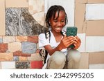 Small photo of young African girl engrossed in her phone, oblivious to her surroundings