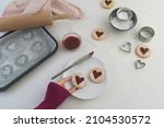 Woman's hand in lower part of frame taking a heart shaped jam filled Linzer cookie. Baking biscuits for valentines day food concept image with white background including copy space.