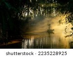 Beautiful view of an asian adult male old boatman rowing a wooden boat with a bamboo stick across a small river stream during sunset to deliver dry grasses for animal feeds in northeast Thailand