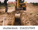Small photo of Excavator working at house construction site - digging foundations for modern house. Beginning of house building. Earth moving and foundation preparation.