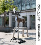 Small photo of Hannover, Germany - sep 13th 2020: Sometimes art and reality are combined in a funny way. Sculpture of a moose manhandling a person has electric scooters lying in front of it.