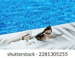 Small photo of Elegant jewellery set of gold earrings and ring with blue topaz with sunglasses near swimming pool with transparent water as a background. Minimal style composition. Product still life concept