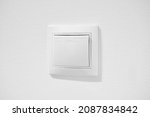 Small photo of Inexpensive plastic push button switch against white wall. White common toggle switch in home. Cheap simple single-pole light switch. Standart rocker switch for exhaust fan or lighting applications