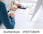 Small photo of Accountant checking financial statement or counting by calculator income for tax form, hands close-up. Business woman sitting and working with colleague at the desk in office. Audit concept