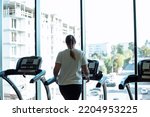 Fat woman alone run on treadmill at fitness gym and look out window at transport traffic and city, back view. Overweight lady do cardio workout on training apparatus. Weight loss, sport lifestyle.
