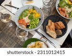 Small photo of Various dishes and glasses with white wine lying on table of French restaurant. Salads with fish, avocado, rice, green beans and mango, bread arranged on plates on repast.