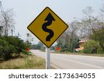 Small photo of Yellow traffic sign with twisty arrow symbol at rural road Thailand to warn drivers be careful when driving on twisty way road. Concept : Warning traffic sign for transportation.
