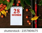 Small photo of calendar date on wooden dark desktop background with autumn leaves and small apples. November 28 is the twenty-eighth day of the month.