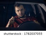 Small photo of A young bearded man fastens his seat belt in a car. Safe driving. Responsible and law abiding driver concept. Driving on highways at night.