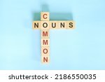 Small photo of Common nouns concept in English grammar education. Wooden block crossword puzzle flat lay in blue background.