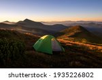 Green camping tent on top of mountain with amazing sunrise on background. Time spending on fresh air. Travelling concept.