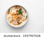 Seafood stew (or creamy soup) in ceramic bowl. Shrimps (prawns), mussles and calamari rings stewed in cream with garlic and green parsley. Healthy mediterranean food top view. White background.