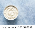 Mascarpone cheese (or cream cheese, ricotta) in white ceramic bowl top view. Ingredient for cooking italian dessert tiramisu. Creamy texture. Copy space. Blue concrete background. 
