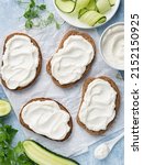 Small photo of Open sandwiches, rye bread bruschetta with cream cheese spread (ricotta) and cucumber slices on white wax paper. Healthy delicious breakfast, lunch or snack food. Top view. Blue background.